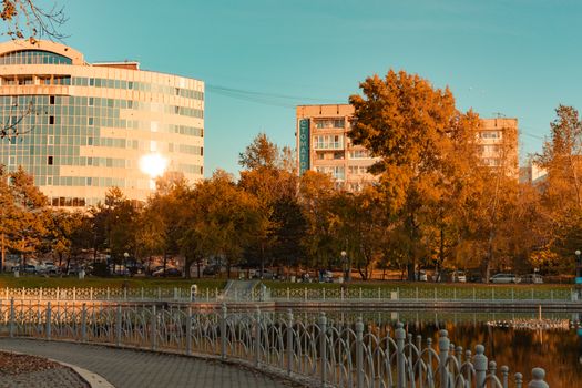 City ponds in the autumn. Trees covered with yellow and orange leaves are reflected in the water. Blue sky.