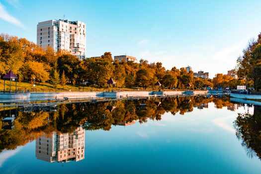 City ponds in the autumn. Trees covered with yellow and orange leaves are reflected in the water. Blue sky.