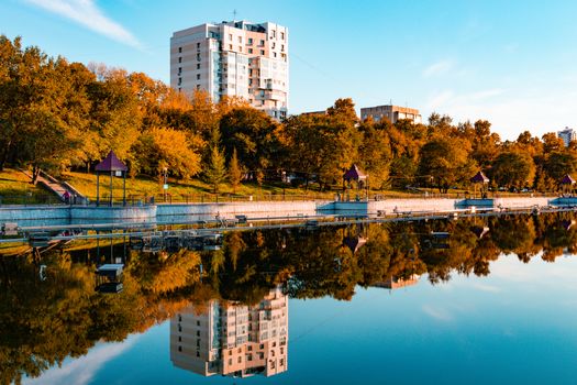 City ponds in the autumn. Trees covered with yellow and orange leaves are reflected in the water. Blue sky.