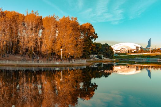 City ponds in the autumn. Trees covered with yellow and orange leaves are reflected in the water. Blue sky.