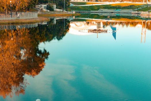 City ponds in the autumn. Trees covered with yellow and orange leaves are reflected in the water. Blue sky.