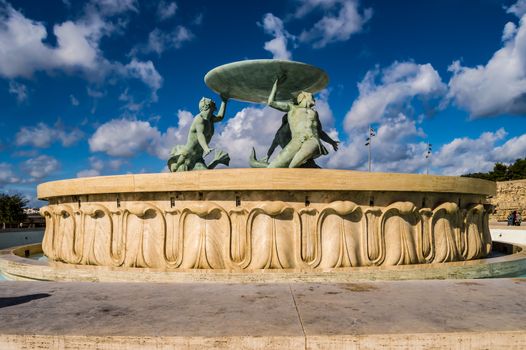 The famous Triton fountain, three bronze Tritons holding up a huge basin, in front of the City Gate in Valletta, sizable landmark fountain featuring multiple bronze tritons on a stone base, Valletta