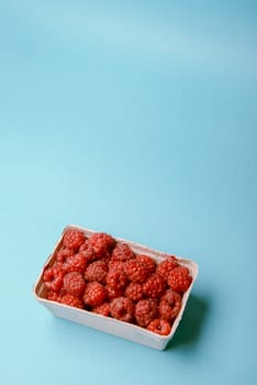 box of fresh raspberries on a blue background