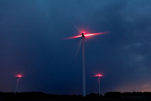 Wind turbines on a dramatic dark blue clouds in the sky. Storm ahead is coming. Red warning light on the windmill