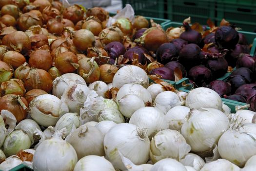 Seasonal vegetables are stacked in boxes at the grocery store. Nearby are yellow, white and red onions. Natural products for cooking healthy food.