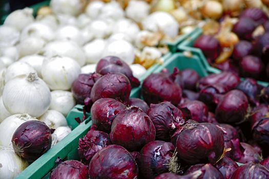 Seasonal vegetables are stacked in boxes at the grocery store. Nearby are yellow, white and red onions. Natural products for cooking healthy food.