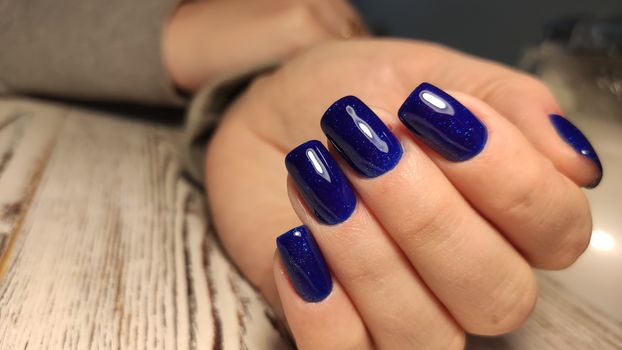 Closeup of hands of a young woman with dark red manicure on nails against white background