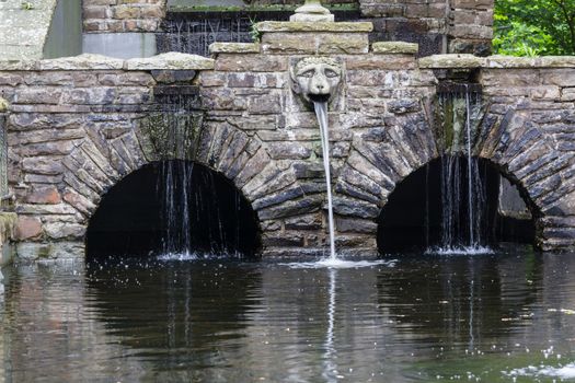 Fountain with waterfall with rock stone decoration in the garden or park. Landscape design detail.