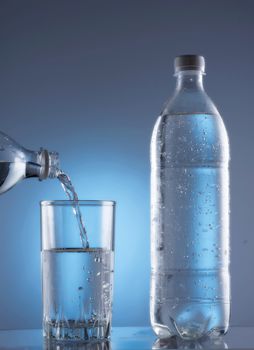 Pouring fresh water from bottle into glass on blue background