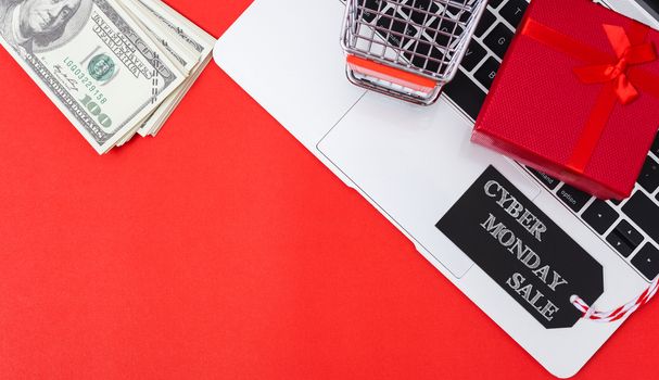 Top view of workspace with black tag, money, gift box and cart shopping on laptop computer on red background and have copy space for use