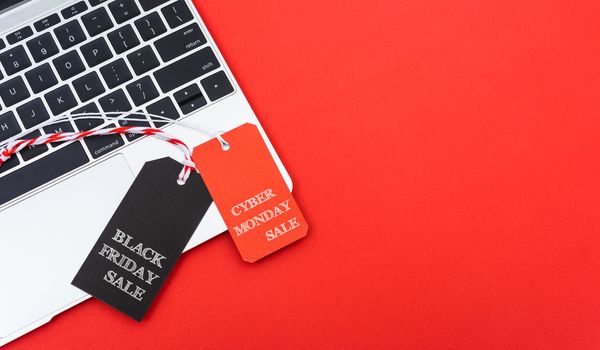 Internet online shopping marketing, top view of workspace with Black Friday text black tag and Cyber Monday text red tag near laptop computer on red background