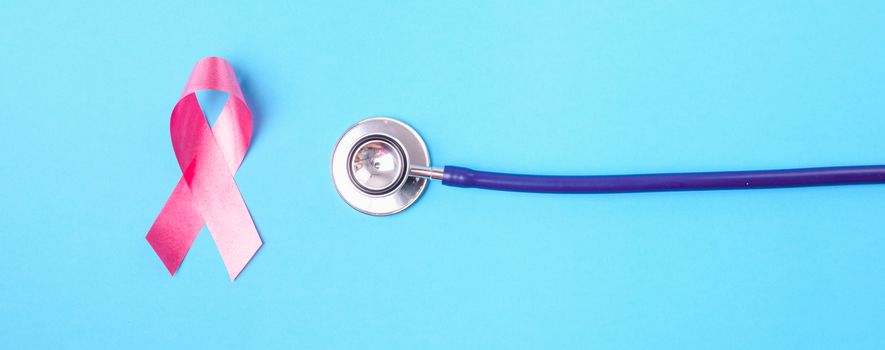 Breast cancer month concept, flat lay top view, pink ribbon and stethoscope on blue background with copy space for your text