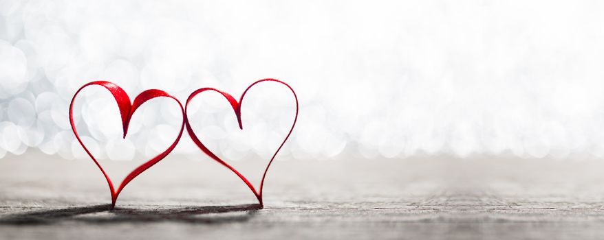 Two red ribbon hearts symbol of love on wooden background with beautiful bokeh, Saint Valentine Day celebration, copy space for text