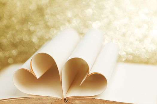 Pages of open book rolled in heart shape on glitter background