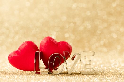 Two red handmade wooden hearts and word love on golden bright glitter lights bokeh background