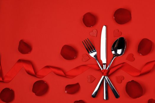 Cutlery set tied with silk ribbon rose flower petals and hearts on red background Valentine day dinner concept
