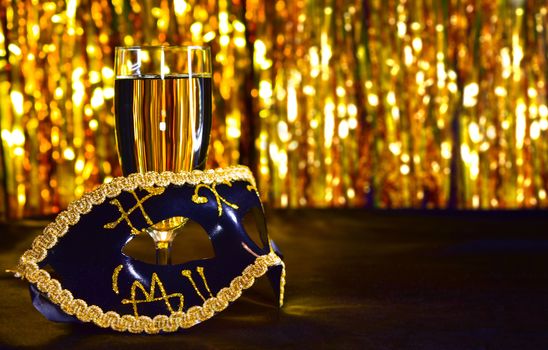 Golden venetian mask with glasses of champagne, on black silk. New year, carnival concept with gold bokeh background. Copy space for the text.