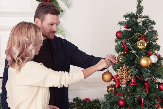 Young couple decorating Christmas tree putting on xmas balls together