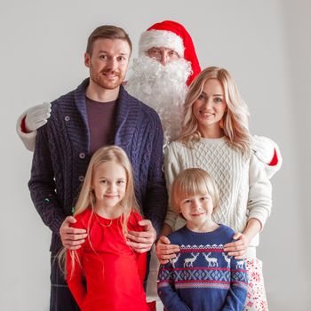 Christmas portrait of happy smiling family with two children and Santa Claus embracing them on gray background