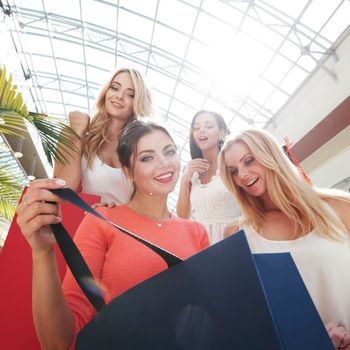 Happy female friends women looking at purchase inside shopping bag