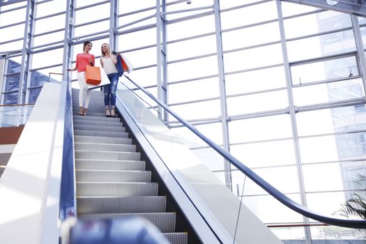 Young beautiful happy women on escalator at shopping mall