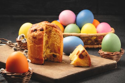 Easter cake on a cutting board and colored eggs on a table and in a wicker basket - traditional Easter breakfast.