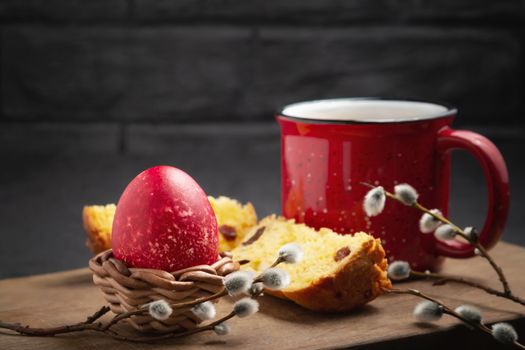 Red Easter egg, a slice of Easter cake and a cup of coffee on a cutting board on a dark table - traditional Easter breakfast.