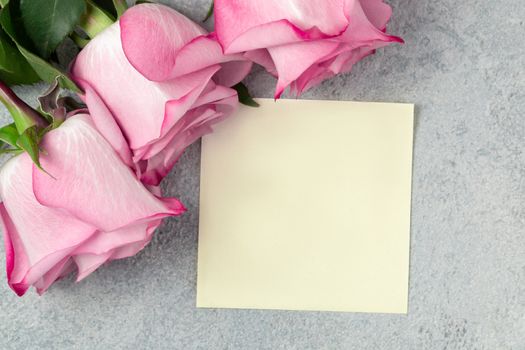 Flower arrangement - a bouquet of pink roses and an empty sheet for a note on a gray concrete surface.