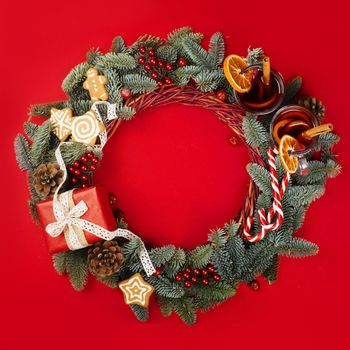Christmas decorative wreath with noble fir tree twigs pine cones gift and mulled wine on red paper background with copy space for text