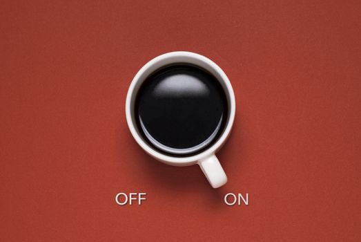 Fun concept of a mug of coffee control switch with off and on text viewed from overhead on a red background