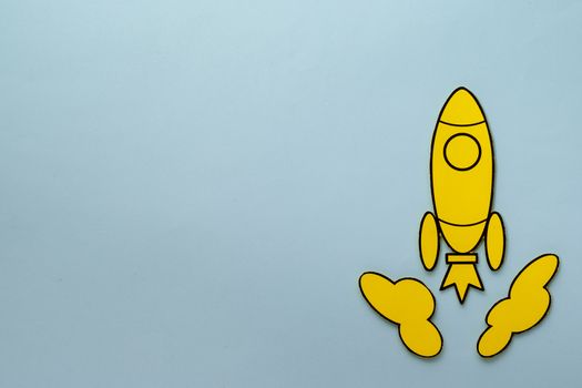 Yellow cartoon rocket zooming through space between two clouds over a blue background with copy space