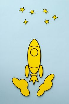 Yellow cartoon rocket flying to the stars zooming through space between the clouds over a blue background with copy space