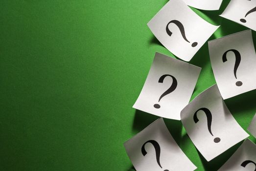 Side border of scattered question marks printed on small white cards curling at the edges over a green background with copy space