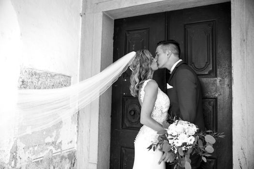 The Kiss. Bride and groom kisses tenderly in front of church portal. Close up portrait of sexy stylish wedding couple kissing. Black and white photo.