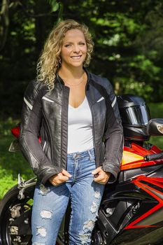 Portrait of a mid-twenties woman, wearing a leather jacket, tank top and jeans in front of a motocycle