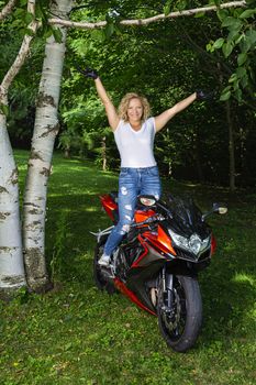 Young woman standing up on her motocycle with her hands in the air