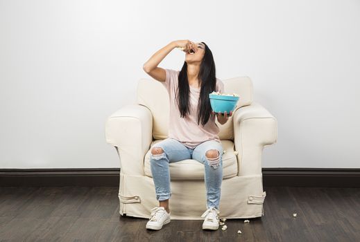 Young woman eating a handfull of popcorn from a blue bowl