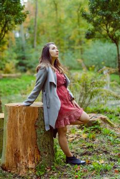 Woman standing next to a tree in park in golden autumn.