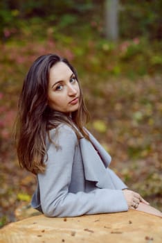 Woman standing next to a tree in park in golden autumn.