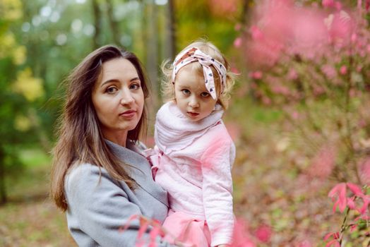 Mother holds daughter in her arms in the park on a sunny day. Autumn day