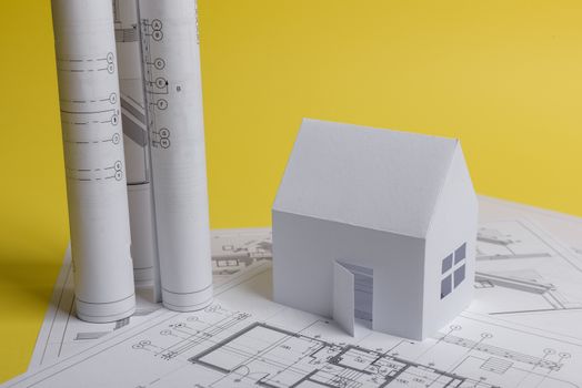 White family paper house, house projects plan and blueprints in the background. Minimalistic and simple concept, style. Horizontal orientation. View from above.