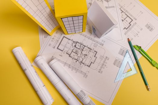 White family paper house, house projects plan and blueprints in the background. Minimalistic and simple concept, style. Horizontal orientation. View from above.
