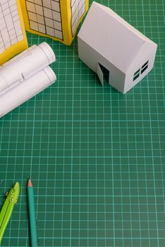 White family paper house, house projects plan and blueprints in the background. Minimalistic and simple concept, style. Horizontal orientation. View from above.