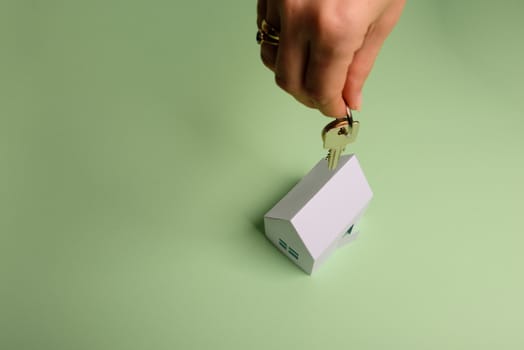 White family paper house. House keys in hand on mint background paper. Minimalistic and simple concept, style. Copy space. Vertical orientation. Family moving or removal concept.