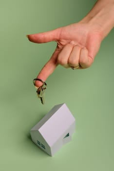 White family paper house. House keys in hand on mint background paper. Minimalistic and simple concept, style. Copy space. Vertical orientation. Family moving or removal concept.