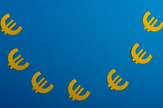 Paper yellow symbols of euro currency on blue background. View from above with copy space