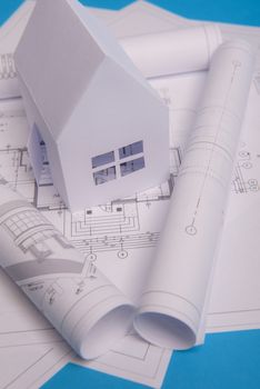 White family paper house, house projects plan and blueprints in the background. Minimalistic and simple concept, style. Horizontal orientation. View from above.