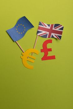 Paper yellow symbols of euro and pound currency on green background. View from above with copy space. EU and United Kingdom flags