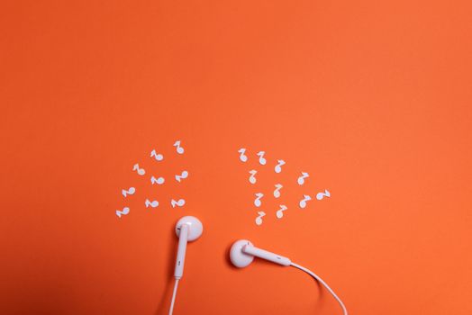 white earphones and white paper notes on orange background. view from above