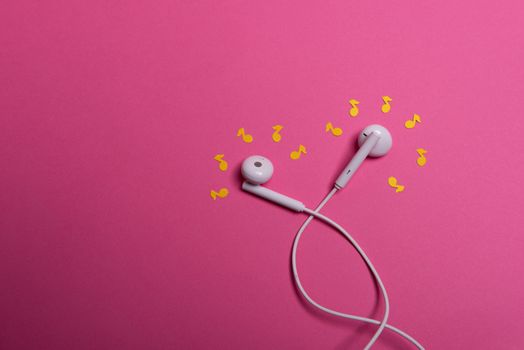 white earphones and yellow paper notes on pink background. view from above